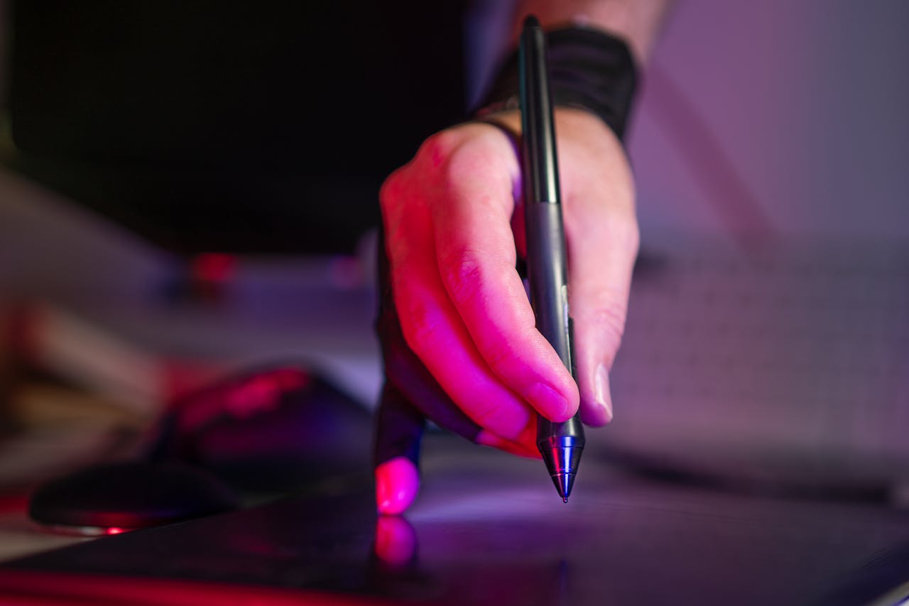 A digital artist's hand working on a graphics tablet with a stylus, in a creative studio setting.