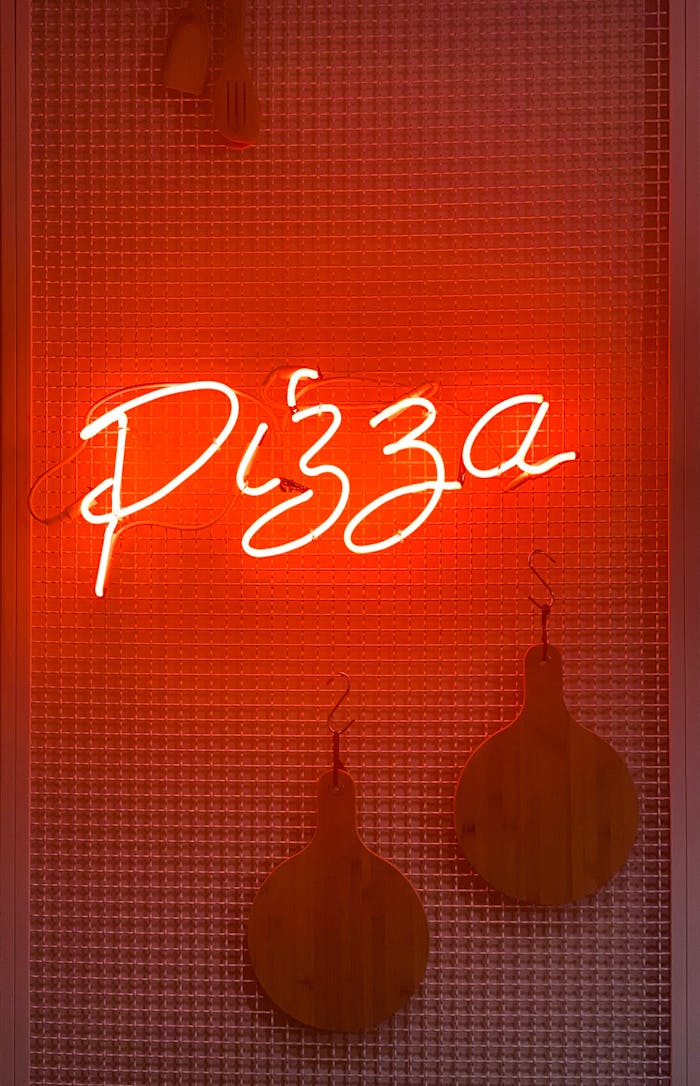 A glowing neon sign displaying the word 'Pizza' on a textured red background.