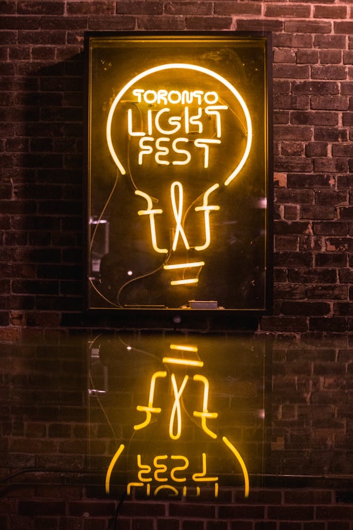 Bright neon sign for Toronto Light Fest against a brick wall, reflecting on a shiny surface.
